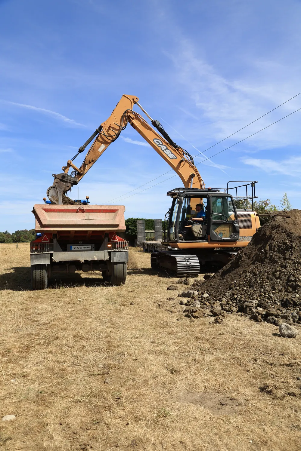 Excavator loading a site trailer beside an earth bank
