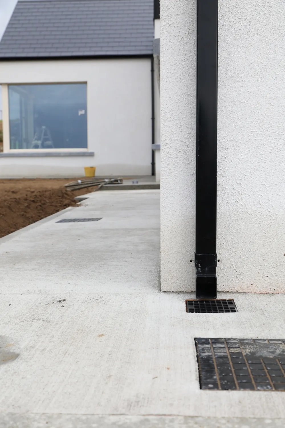 Concrete path meeting a drainage channel beside a house wall