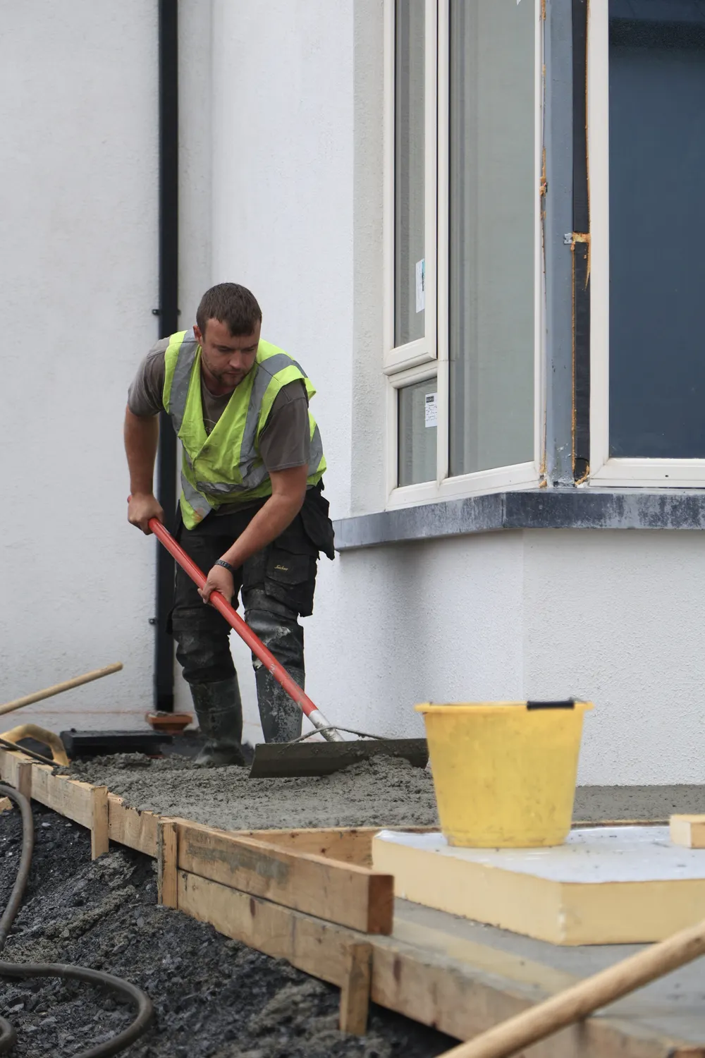 Worker smoothing a concrete path beside a newly built house