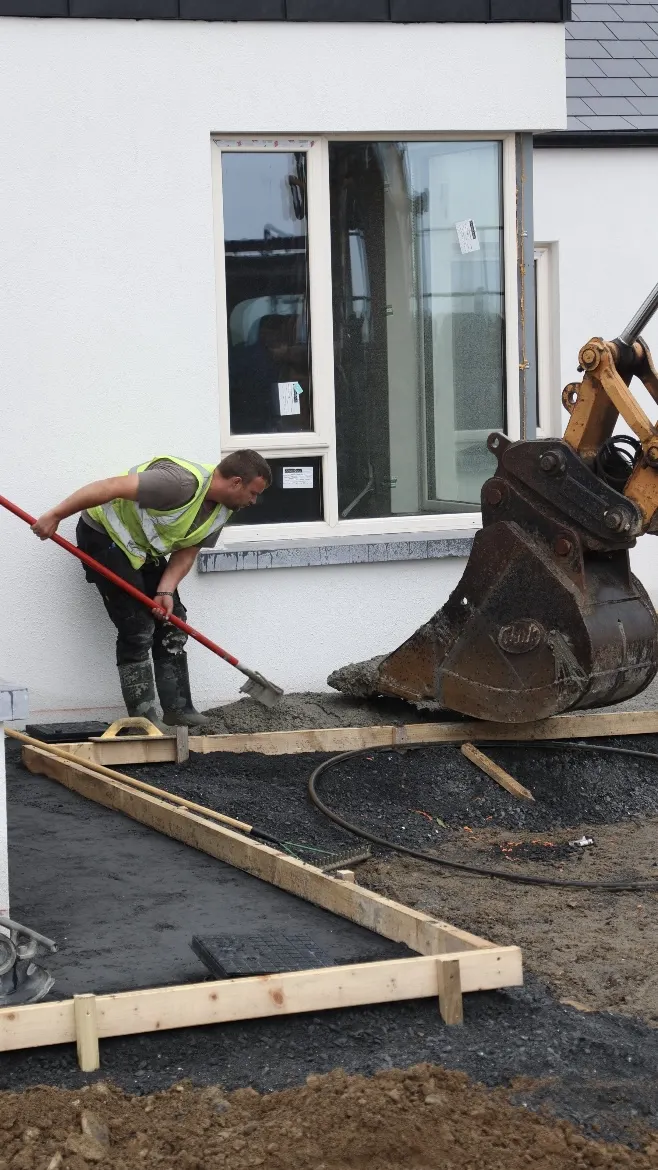 Worker spreading material within timber formwork beside a house