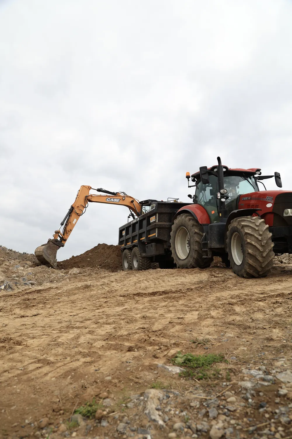 Excavator digging beside a tractor and trailer on an open site