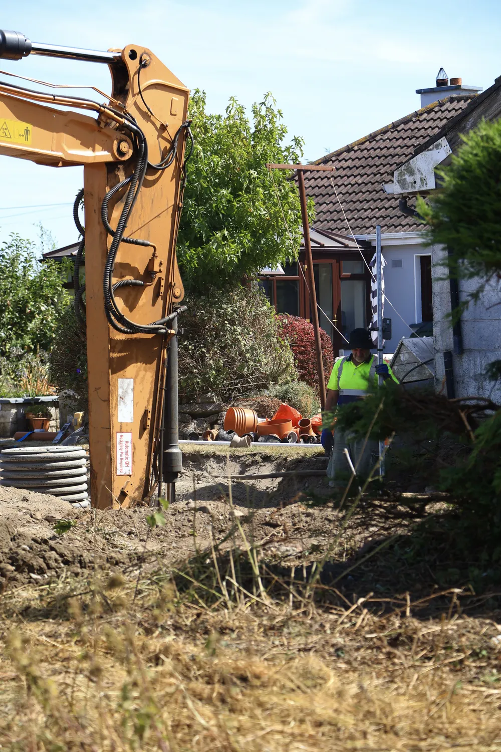 Excavator clearing vegetation and earth around an existing house
