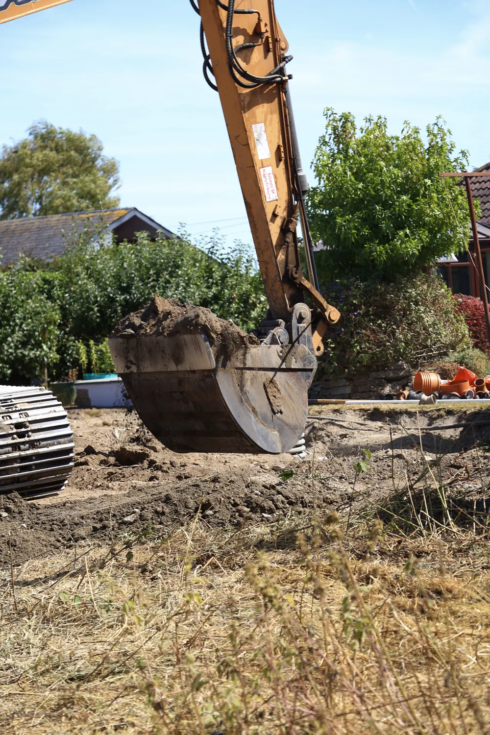 Excavator bucket lifting roots and soil from a garden site