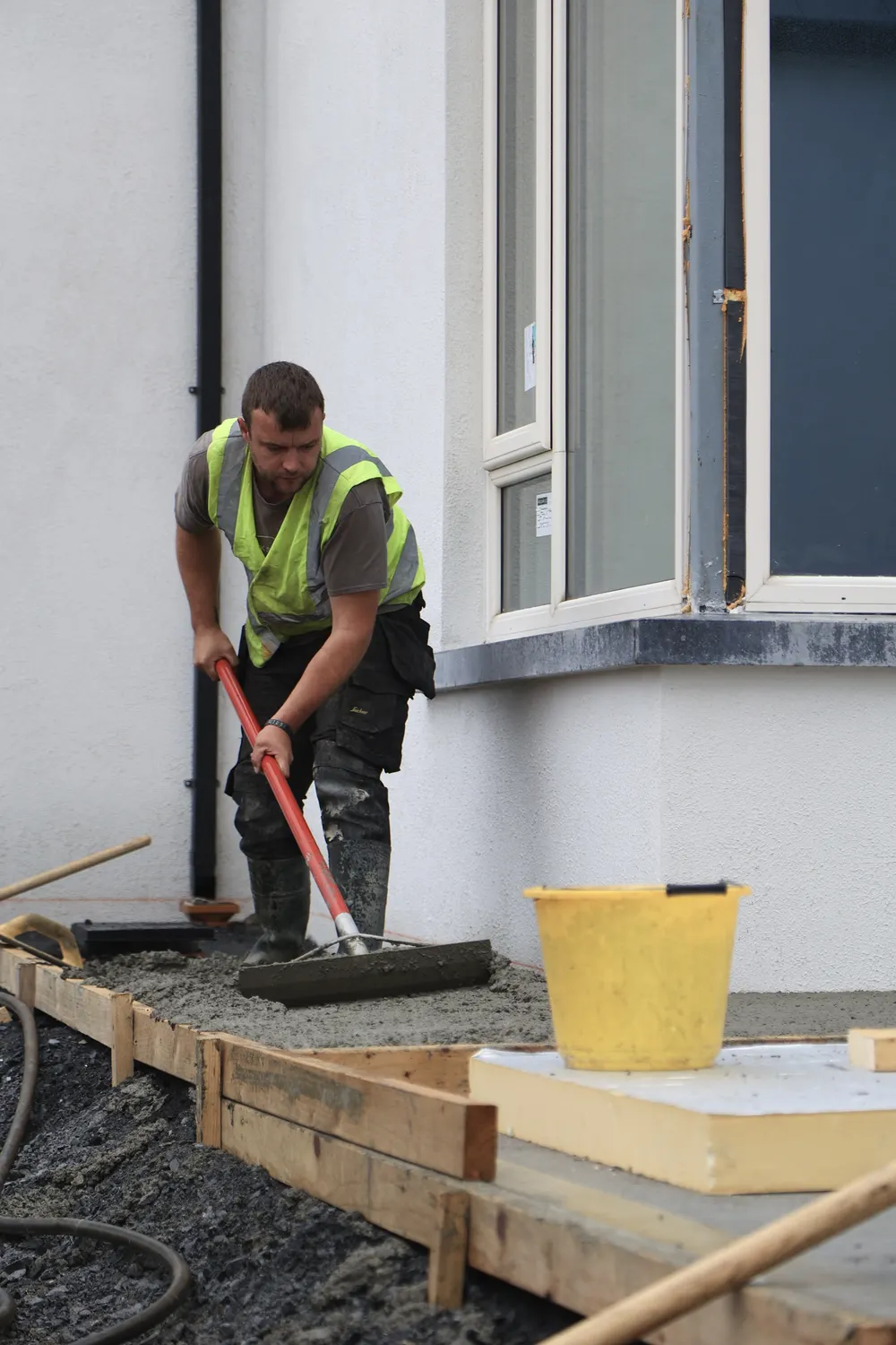 Worker shaping a fresh concrete surface beside a house doorway