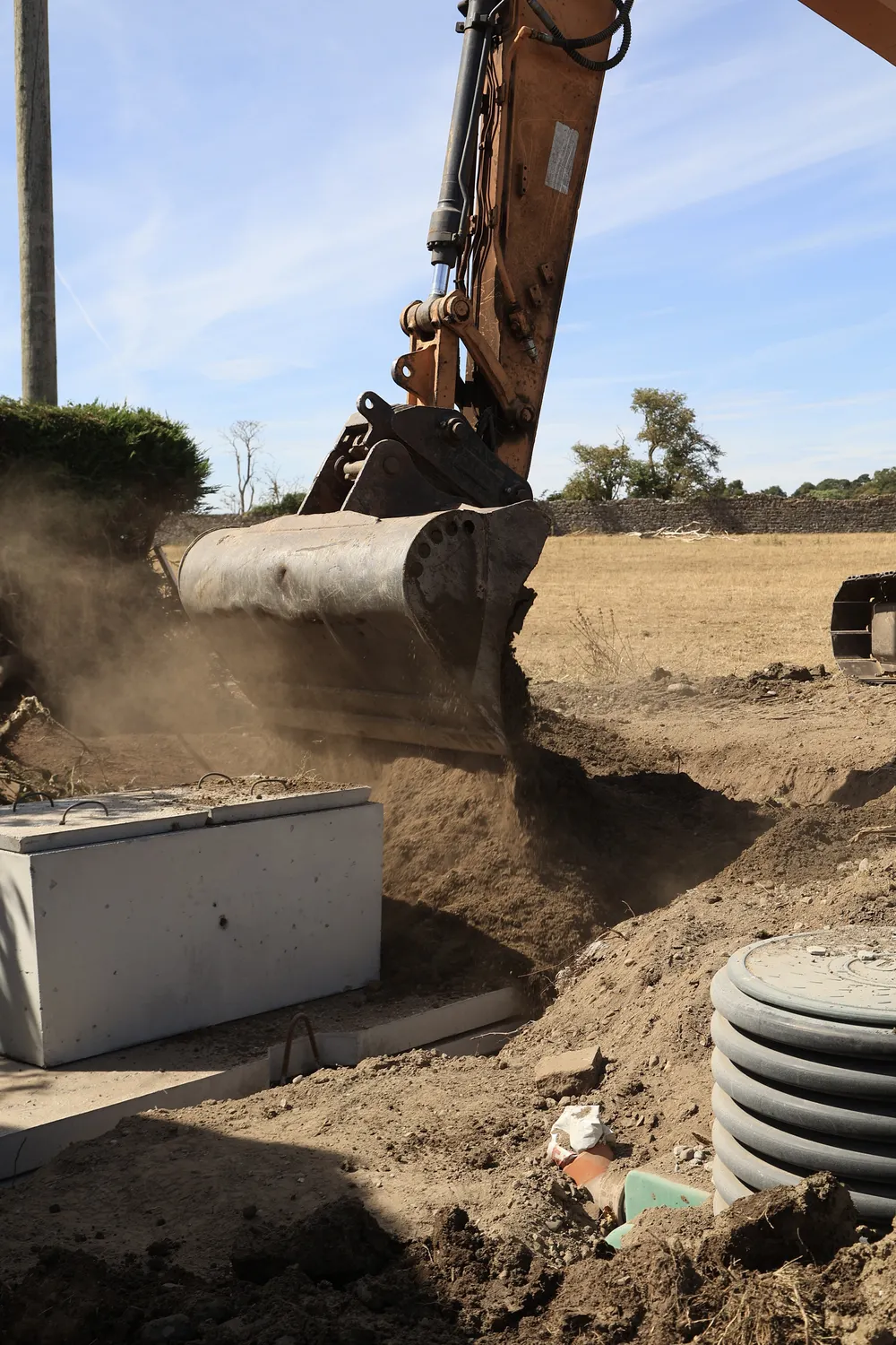 Excavator moving soil alongside a precast tank in a garden