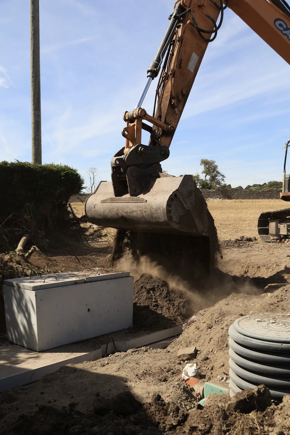 Excavator positioning a concrete tank on prepared ground