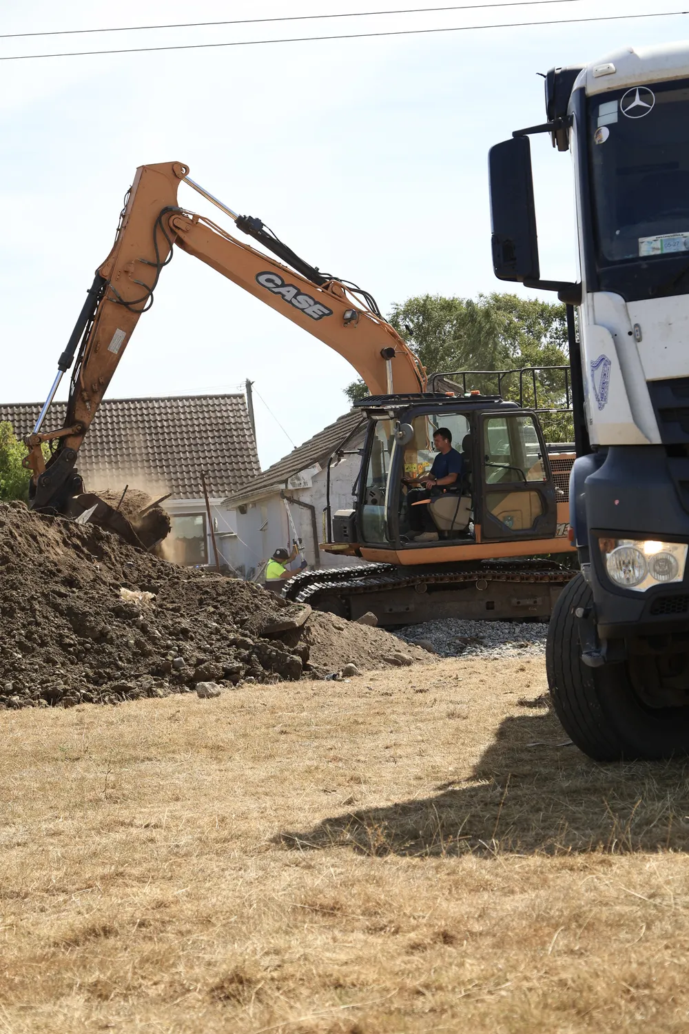 Excavator digging beside a house with a tipper lorry nearby