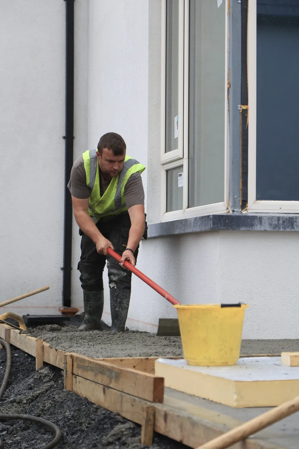 Worker levelling concrete along the edge of a house