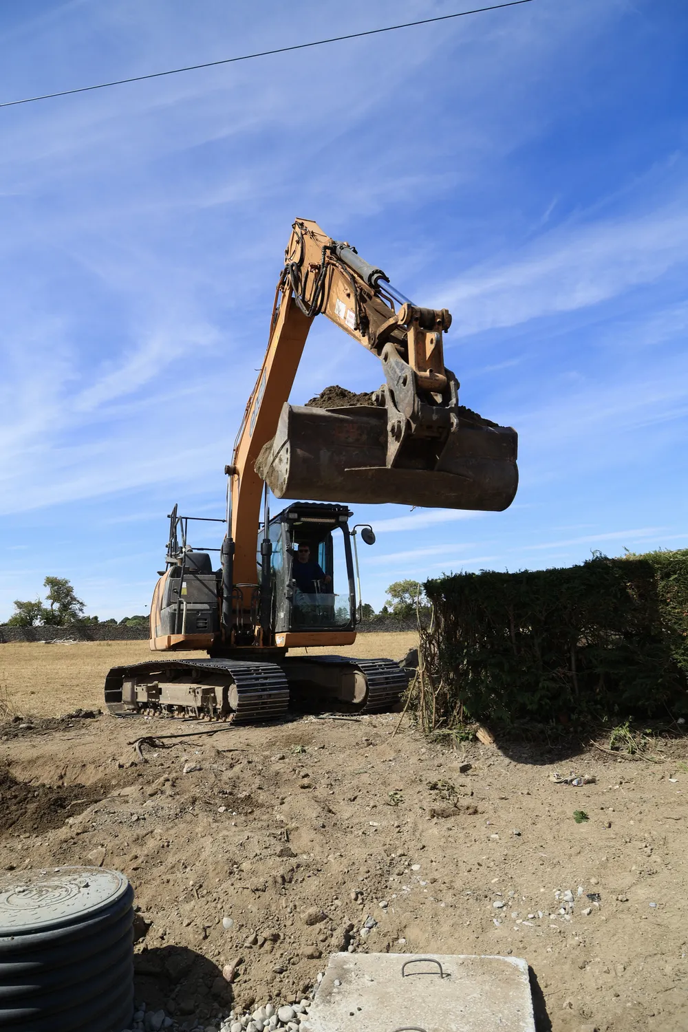 Excavator lifting a full bucket of soil above graded ground