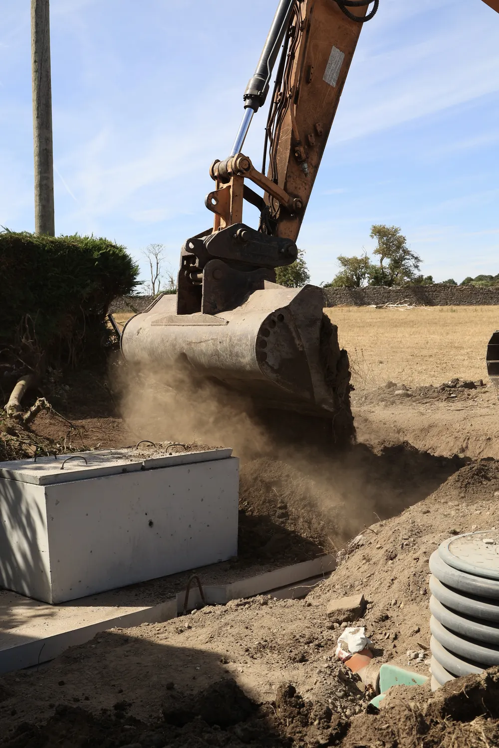 Excavator bucket working beside a precast concrete tank