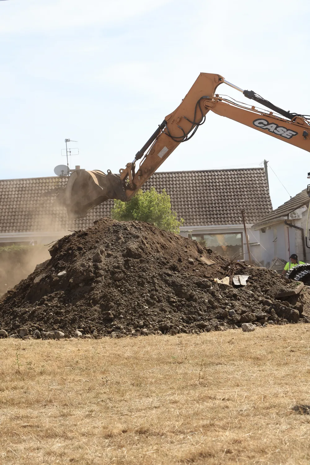Excavator working through a mound of soil on an open site