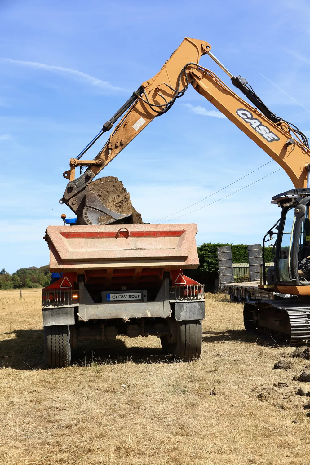 Excavator filling a tipper trailer with earth on a cleared plot